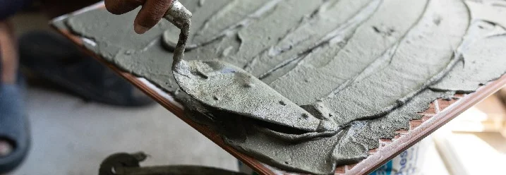 Person verteilt Kleber mit Kelle auf Fliese